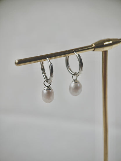 Silver hoop earrings with pearl drops on a gold stand against a gray background