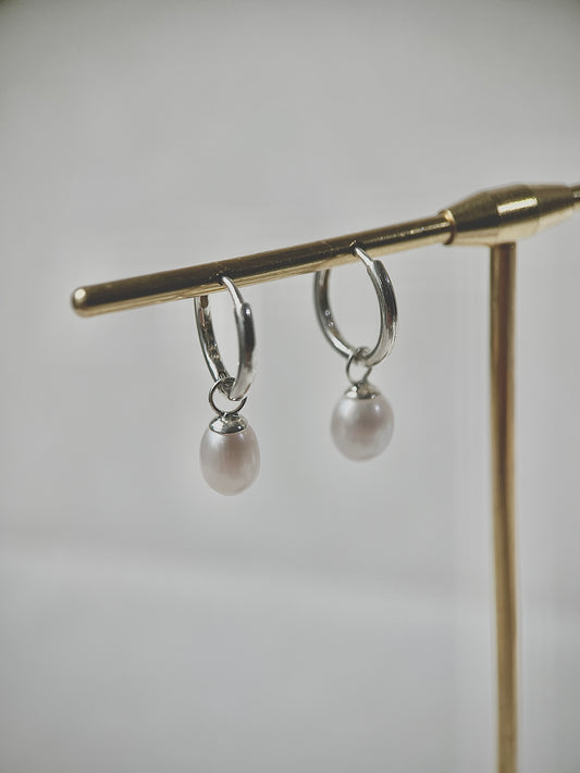 Silver hoop earrings with pearl drops on a gold stand against a gray background