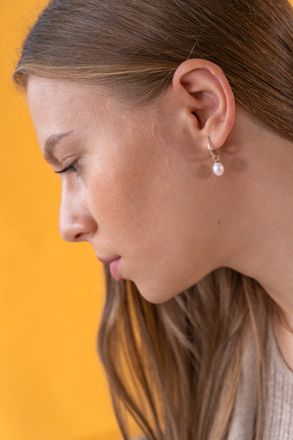 Close-up of a woman wearing white freshwater pearl earrings against a yellow background