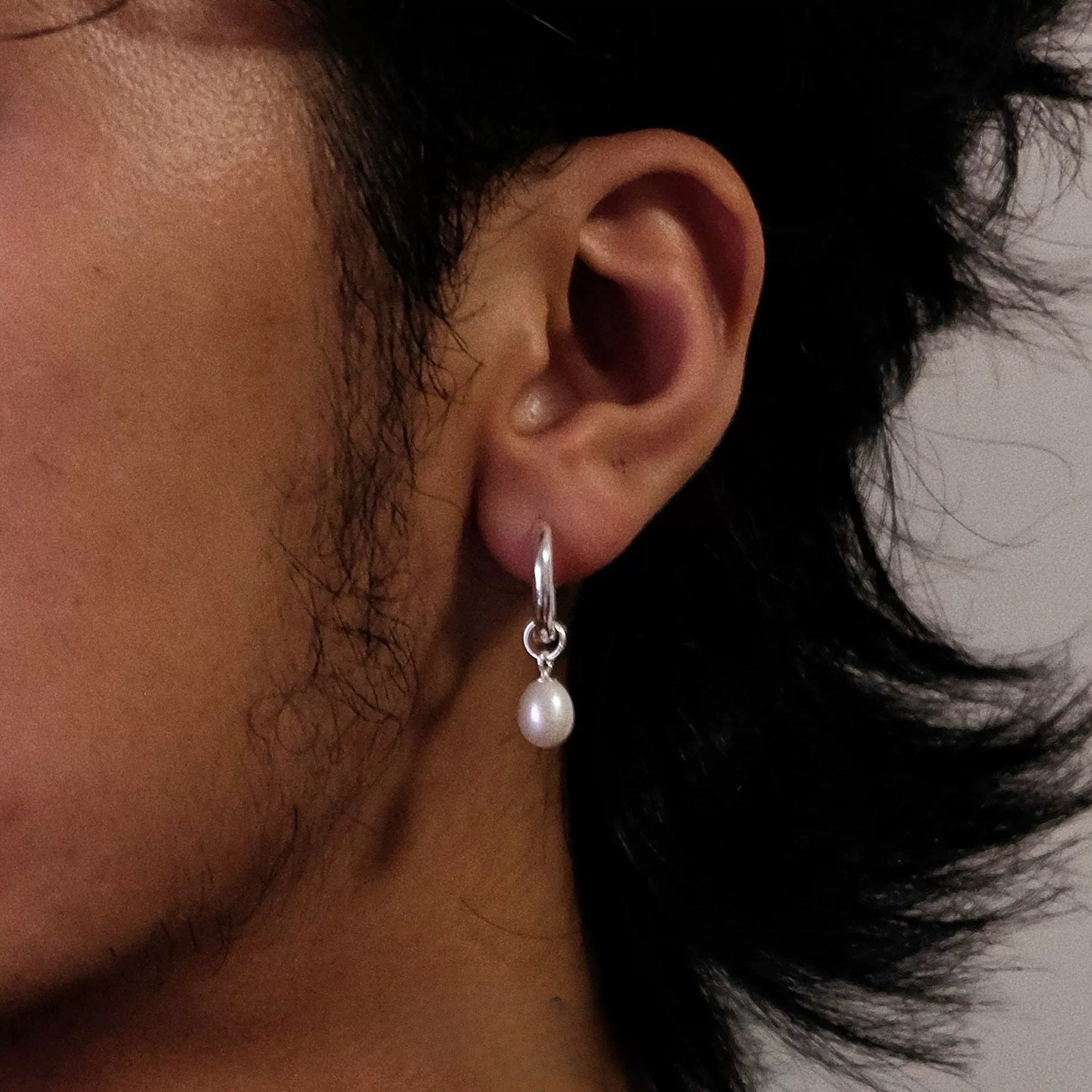Close-up of an ear wearing a pearl earring with a neutral background