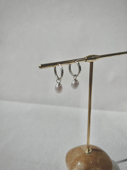 Pair of silver hoop earrings with pearl drops on a gold stand against a white background