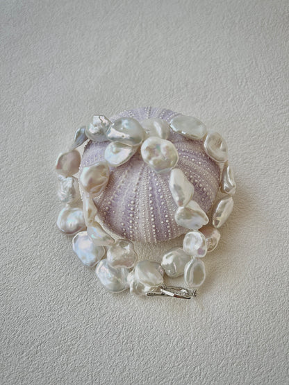 Necklace with pearls and a central shell-like design on a light gray background
