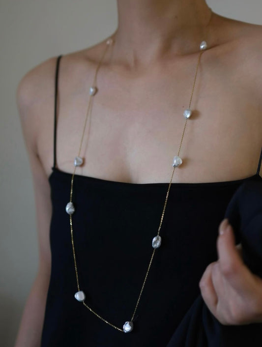 Person wearing a long necklace with keshi pearl beads on a plain background