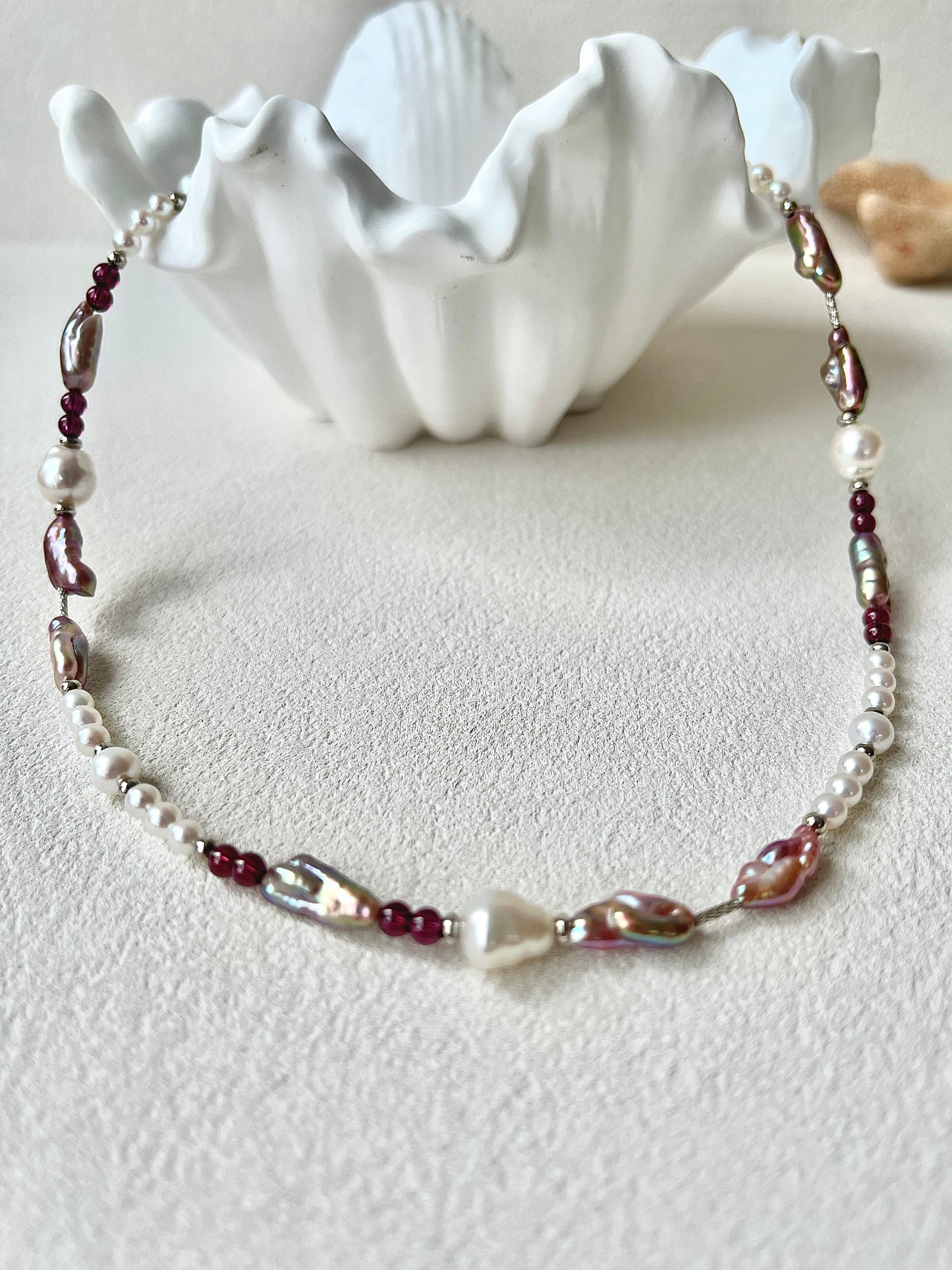 Necklace with pearls and red beads on a white surface with a shell in the background