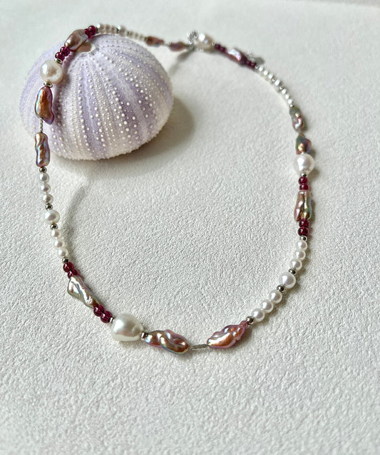 Necklace with mixed pearls and red beads on a textured white surface