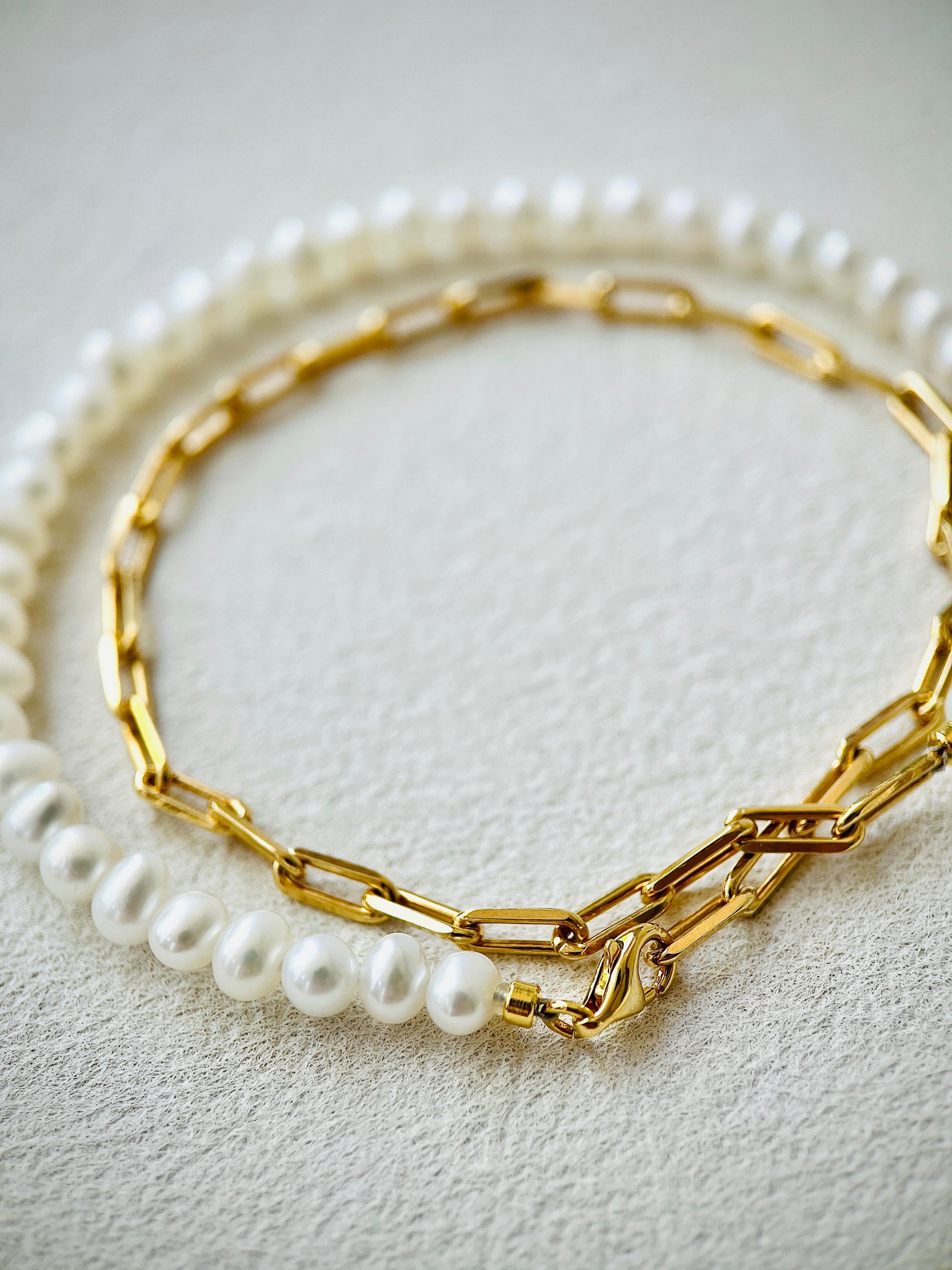 Gold chain bracelet with pearl accents on a light gray background