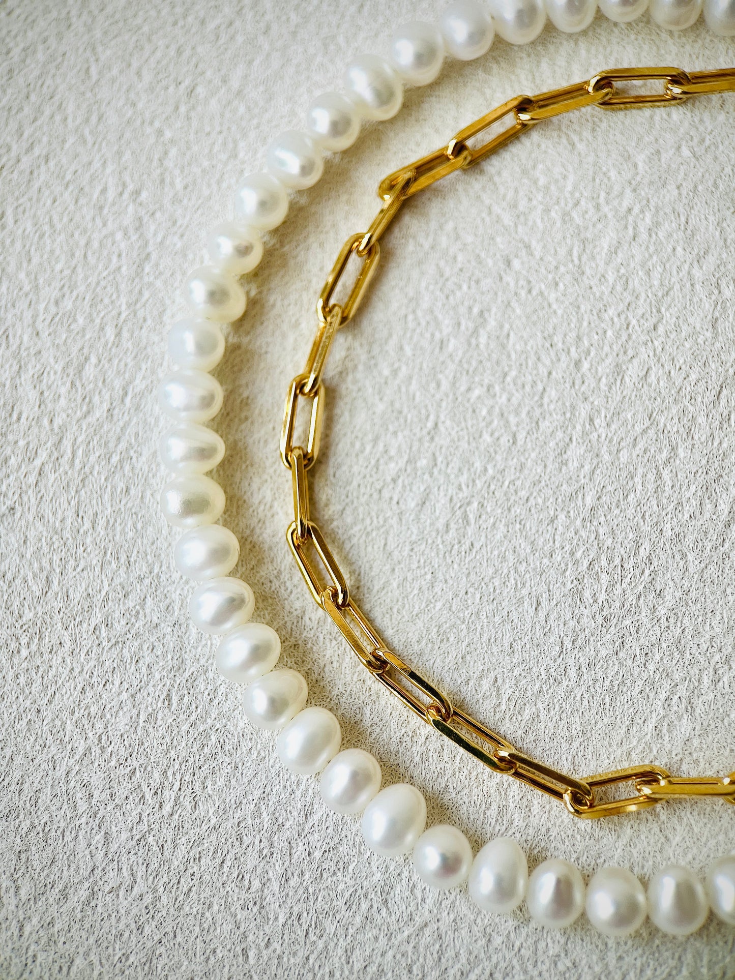 Gold chain necklace and pearl necklace on a textured beige surface