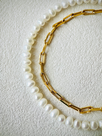 Gold chain necklace and pearl necklace on a textured beige surface