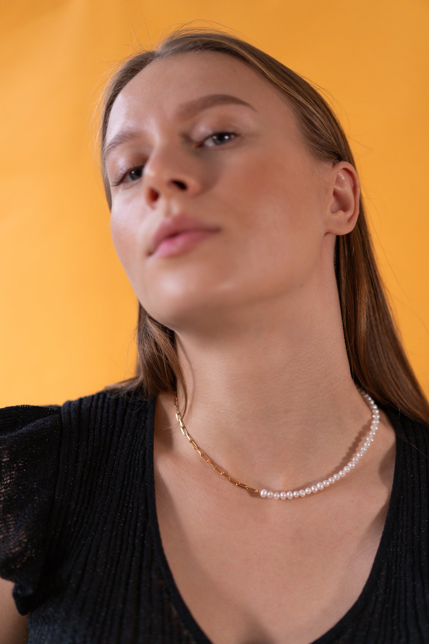 Woman wearing a half pearl half chain necklace against an orange background