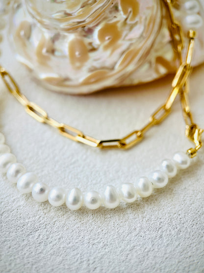 Gold chain necklace and pearl necklace on a textured surface