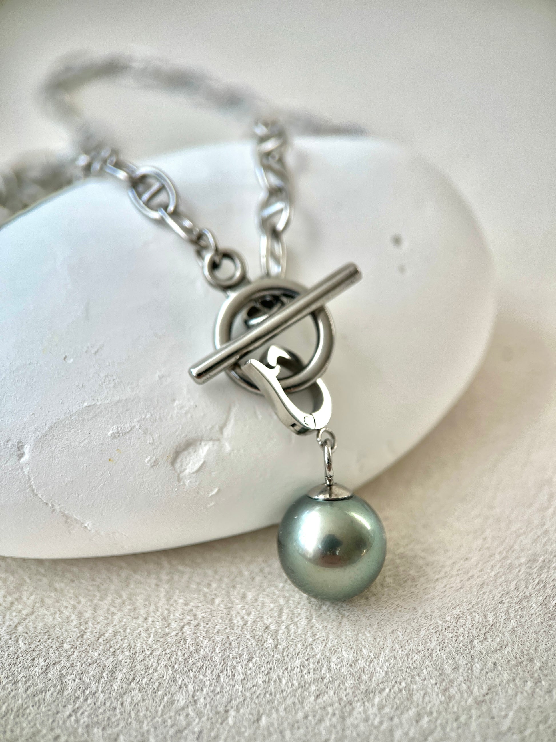 Silver necklace with a single pearl pendant on a white stone background