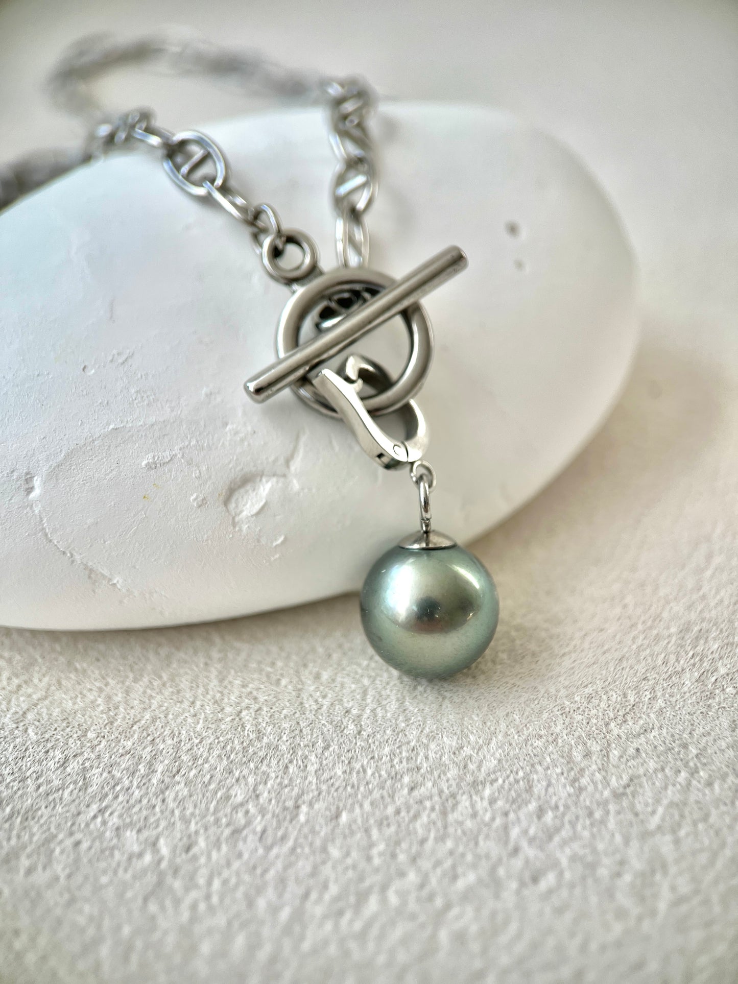 Silver bracelet with a single pearl pendant on a white stone background