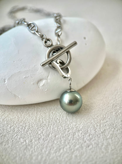 Silver bracelet with a single pearl pendant on a white stone background