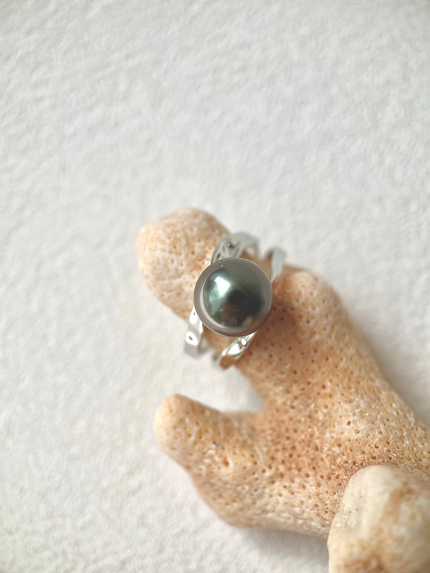Silver ring with a large black Tahitian pearl gemstone on a textured beige surface