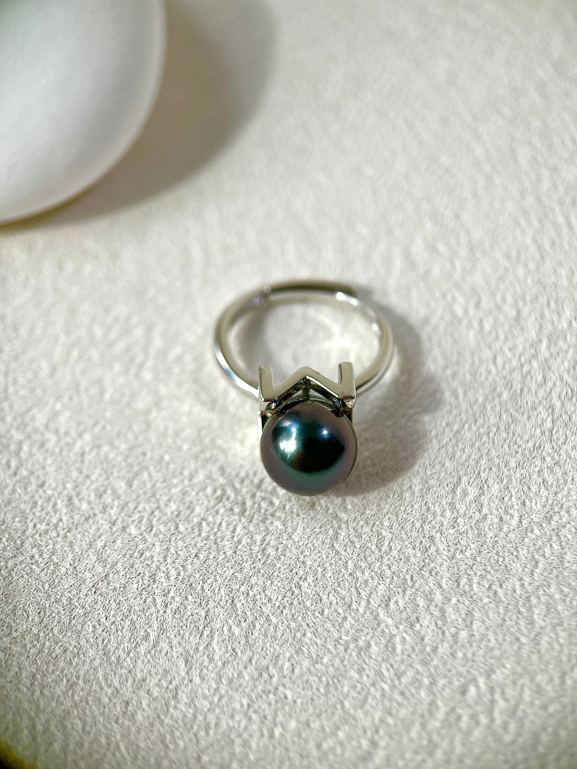 Silver ring with a black pearl on a white surface