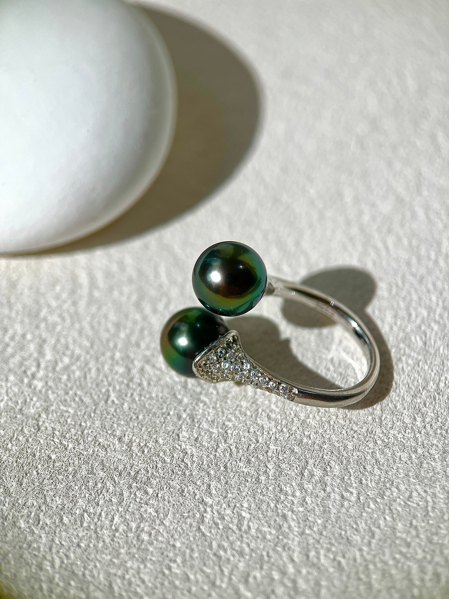 Silver ring with two black pearls on a textured white surface