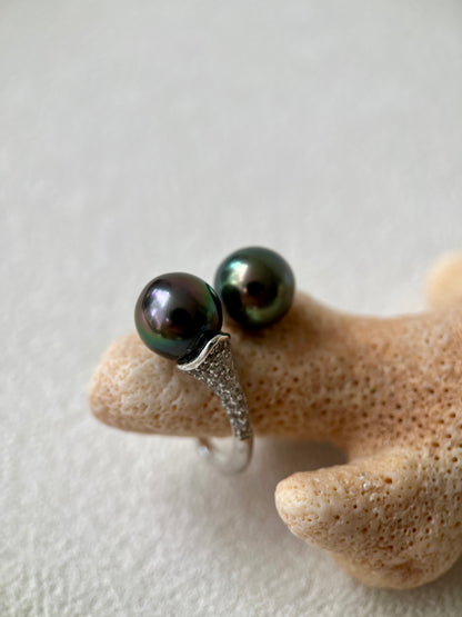 Silver ring with black pearls on a textured beige surface
