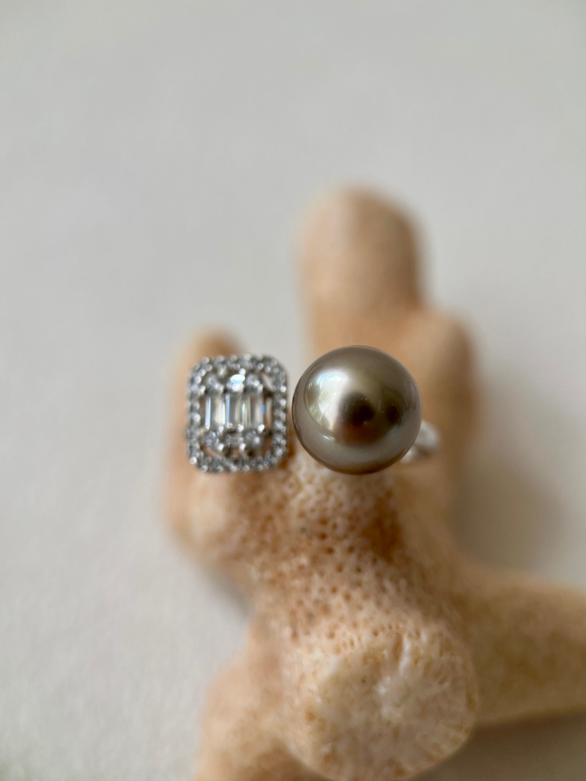 Silver ring with a large tahitian black pearl and smaller gemstones on a textured beige surface