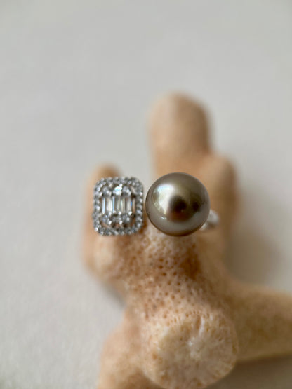 Silver ring with a large tahitian black pearl and smaller gemstones on a textured beige surface