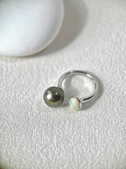 Silver ring with a black pearl and a small white stone on a textured white surface