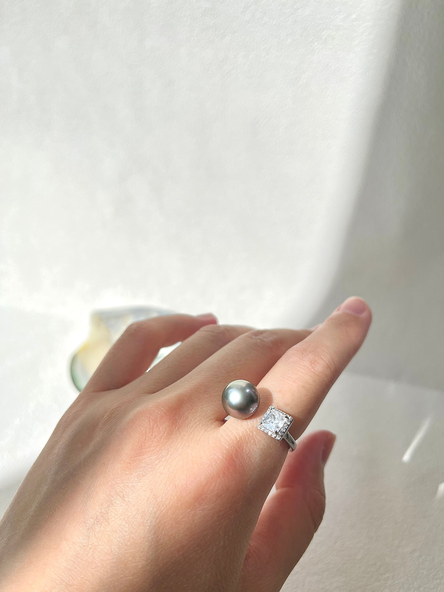 Hand wearing a Tahitian pearl ring with a diamond on a white background