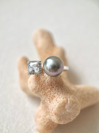 Silver ring with a large Tahitian pearl and smaller diamond on a beige coral background
