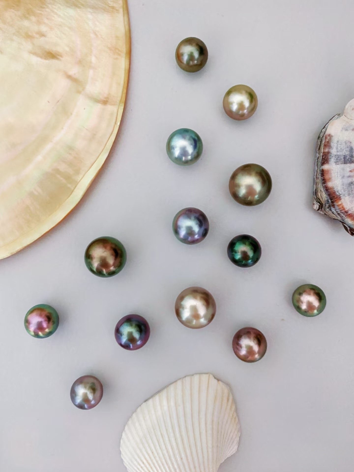 Multicolored pearls on a light gray surface with seashells.
