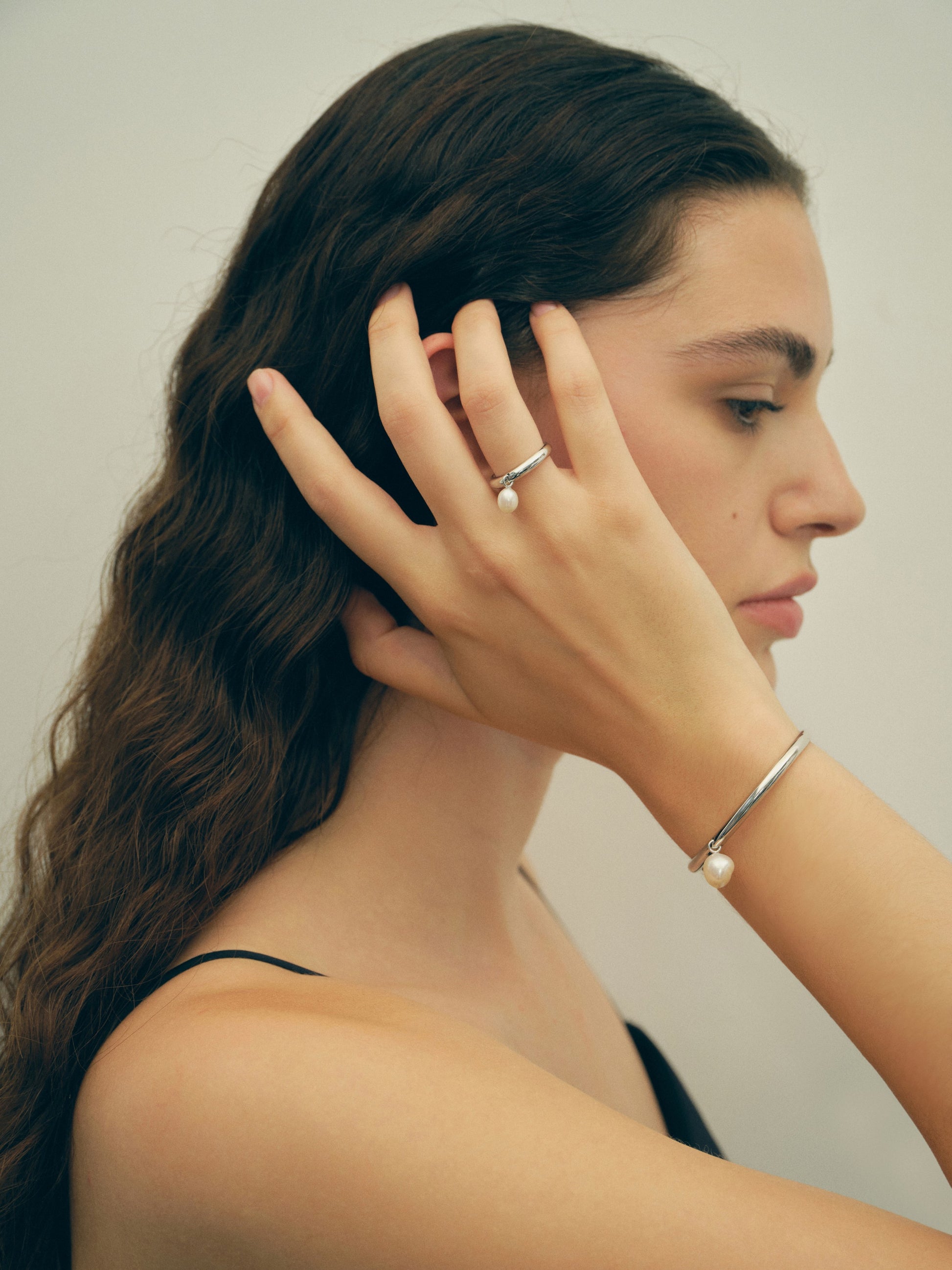 Woman wearing pearl jewelry against a neutral background