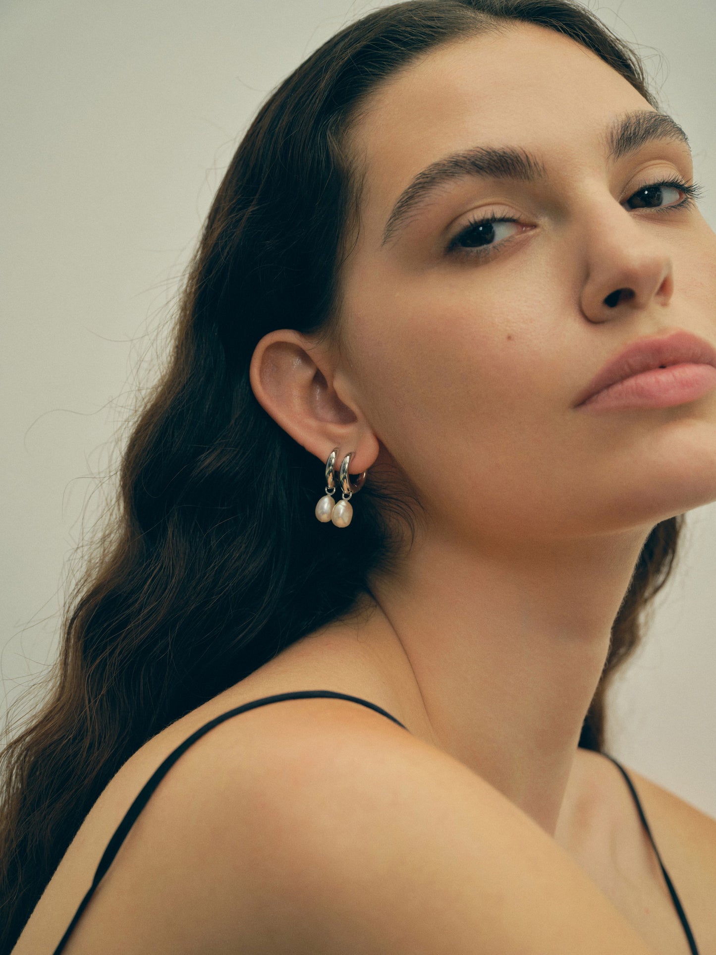 Close-up of a woman wearing white pearl earrings against a neutral background