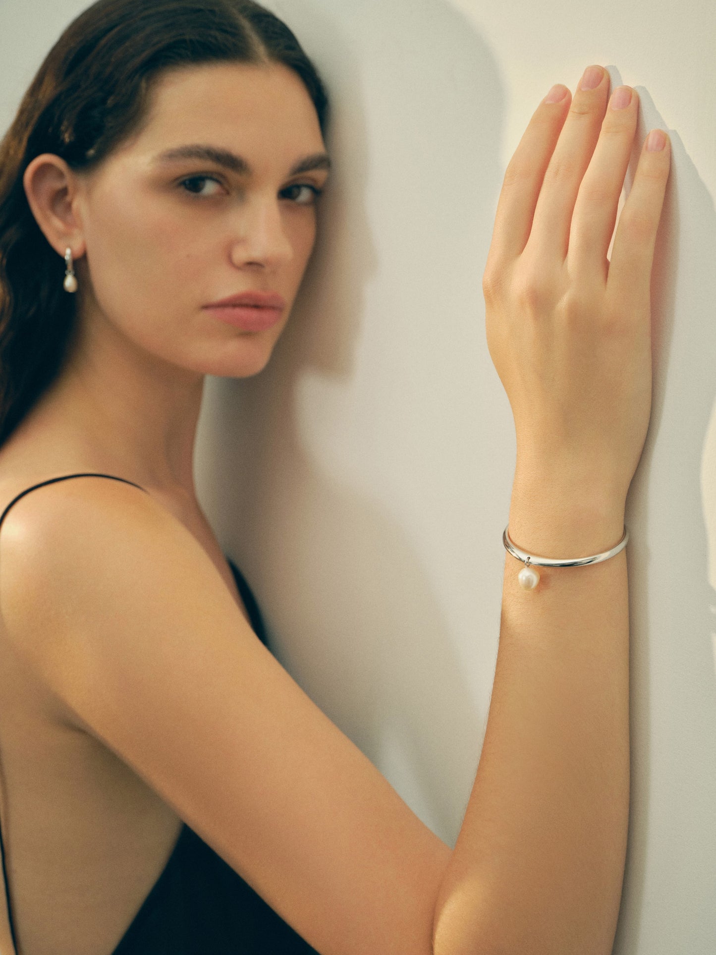 Woman wearing a pearl bracelet and earrings against a plain background