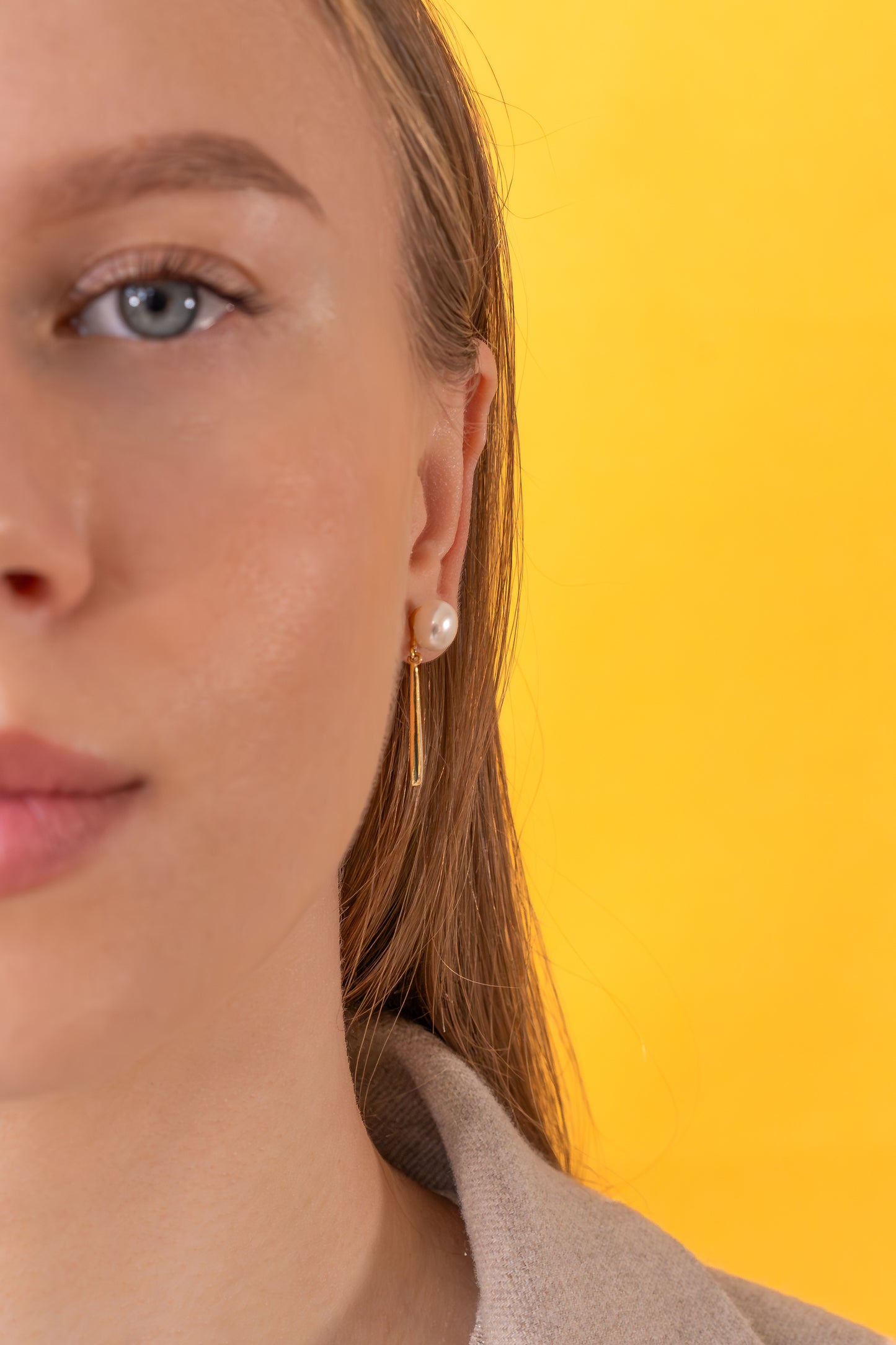 Close-up of a person wearing pearl earrings with a yellow background