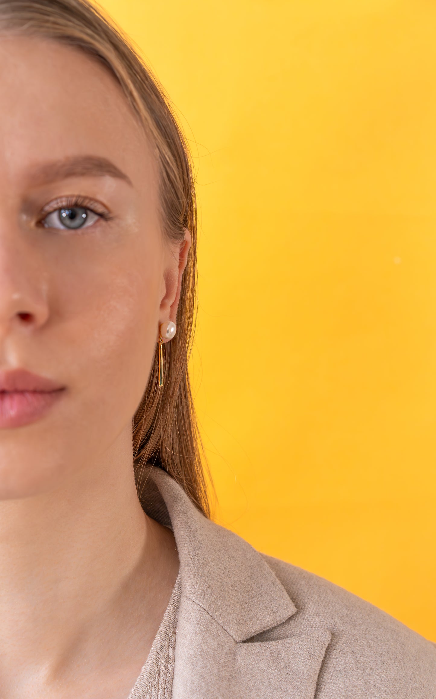 Woman wearing a beige blazer and gold pearl earrings against a yellow background