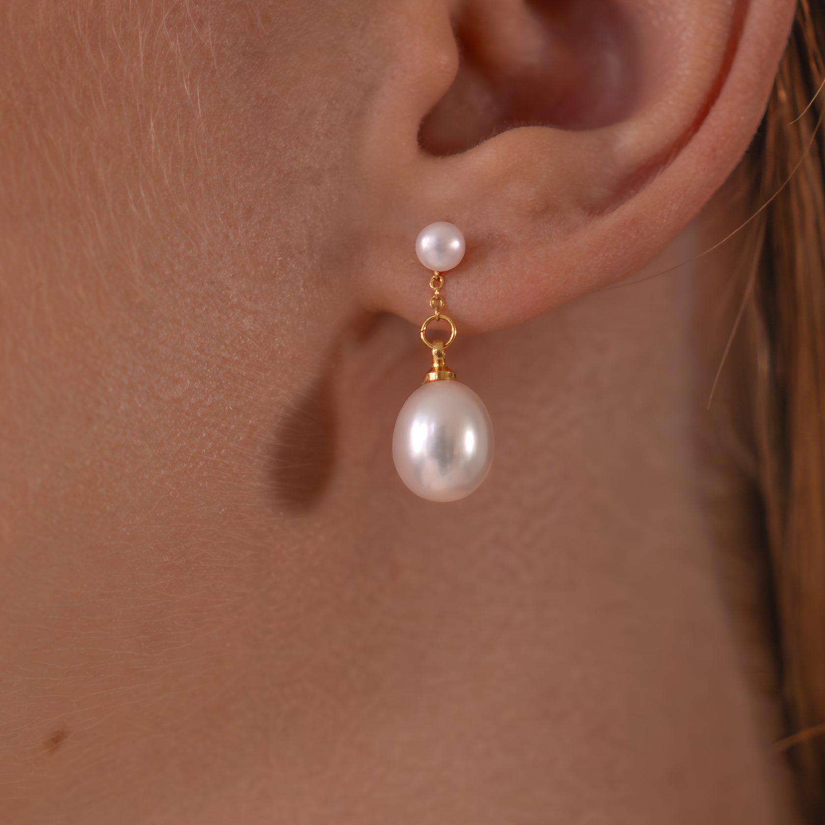 Pearl earring worn on an ear with a plain background