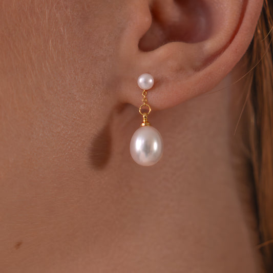 Pearl earring worn on an ear with a plain background