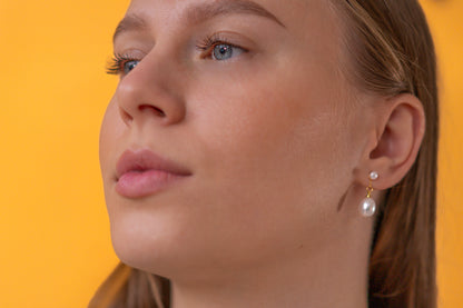 Close-up of a woman wearing pearl earrings against a yellow background