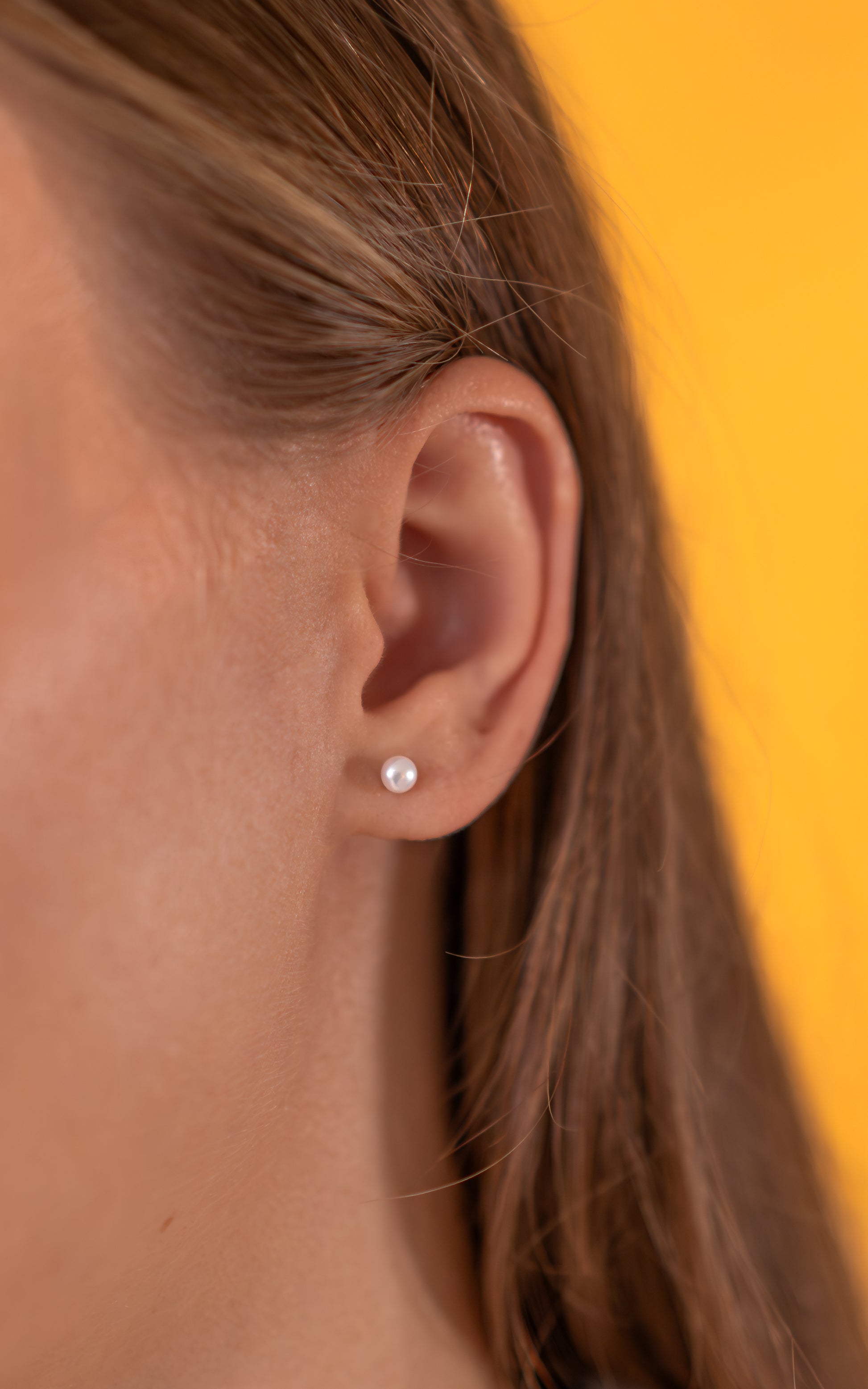 Close-up of an ear with a pearl stud earring against a yellow background