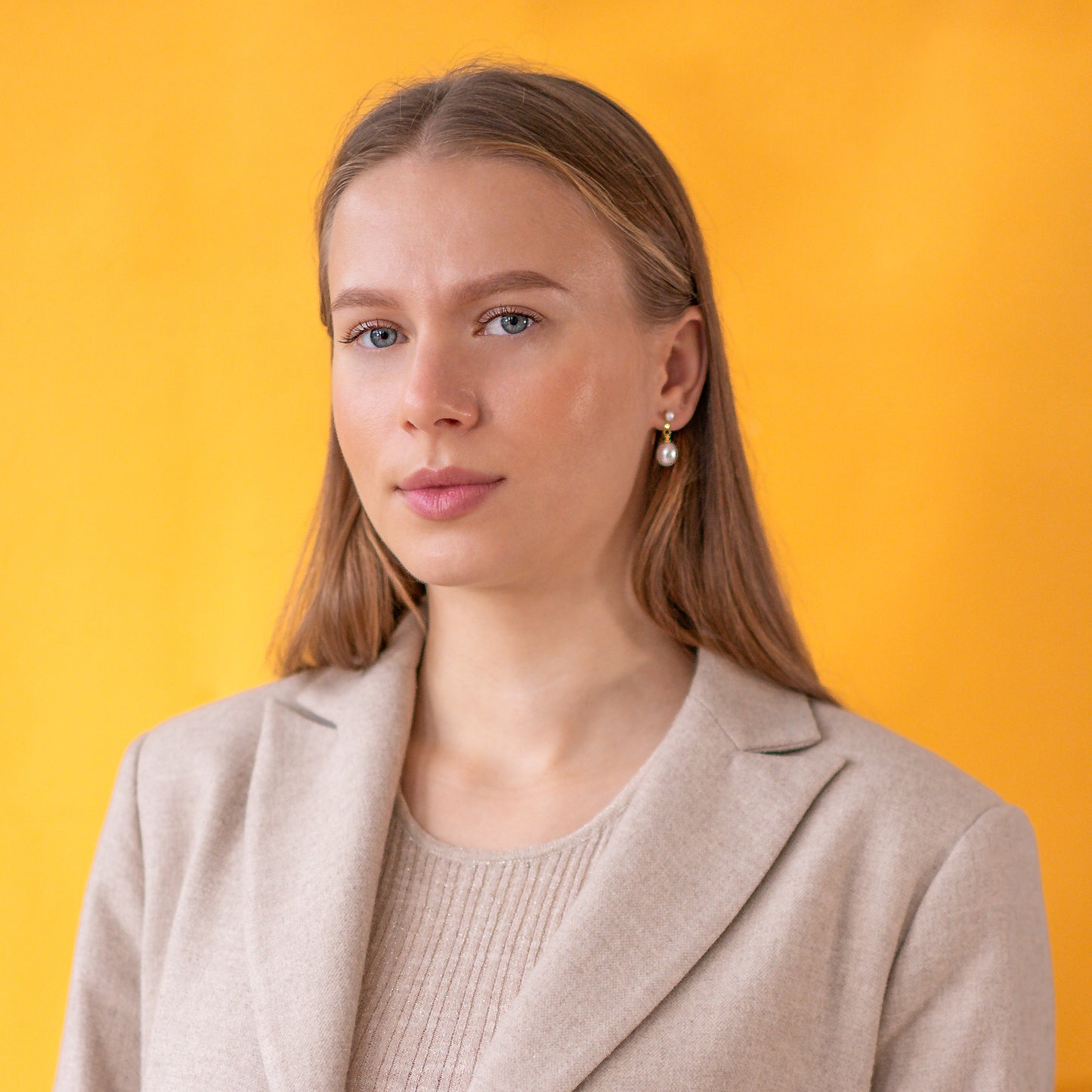 Woman wearing gold pearl earrings against a yellow background