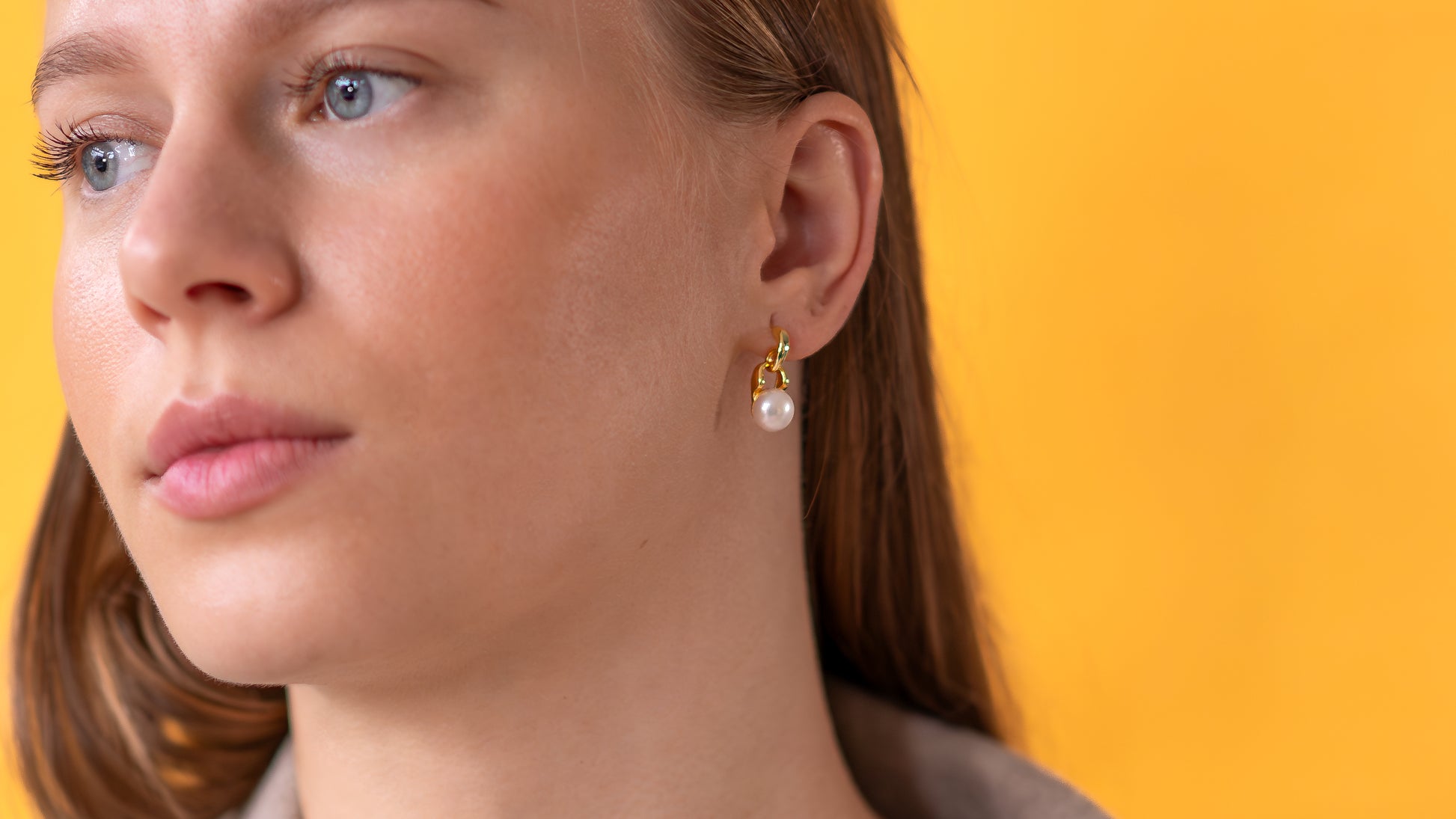 Close-up of a woman wearing pearl earrings against a yellow background