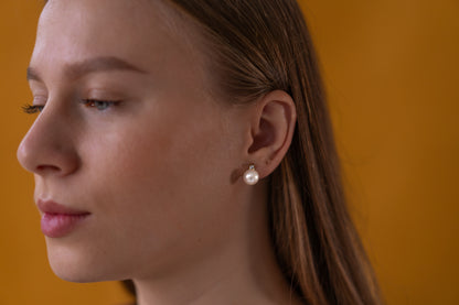 Close-up of a female model wearing pearl earrings against a mustard yellow background