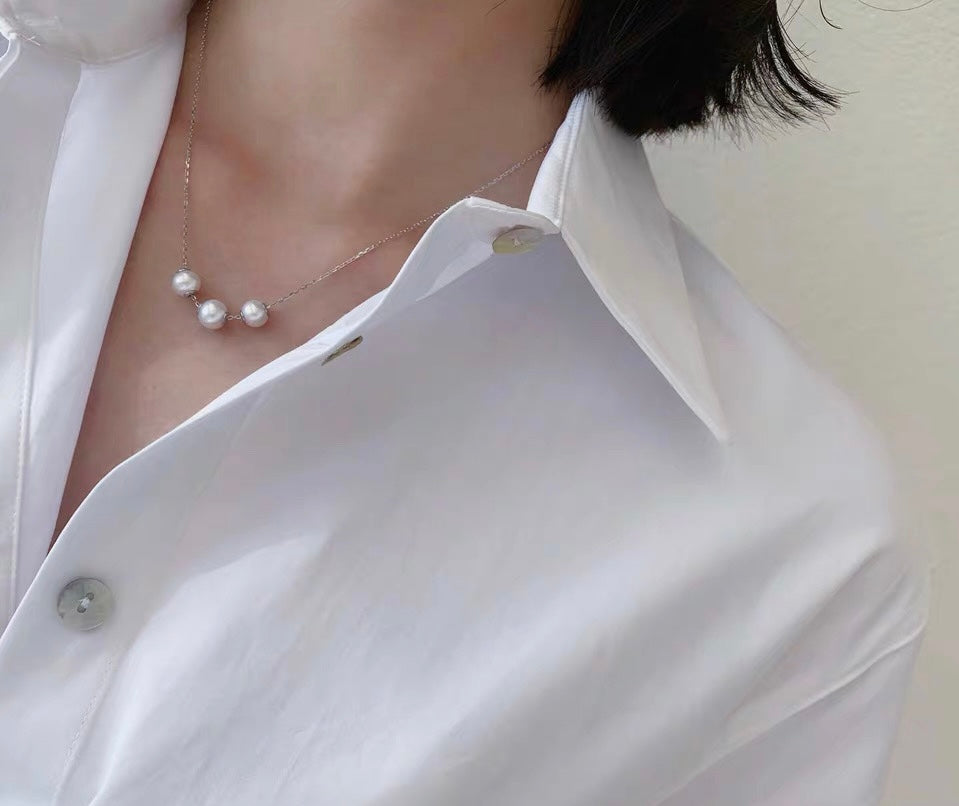 Woman wearing adjustable freshwater pearl necklace with three round pearls on a white shirt.