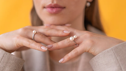 Close-up of a woman's hands wearing pearl rings against a yellow background