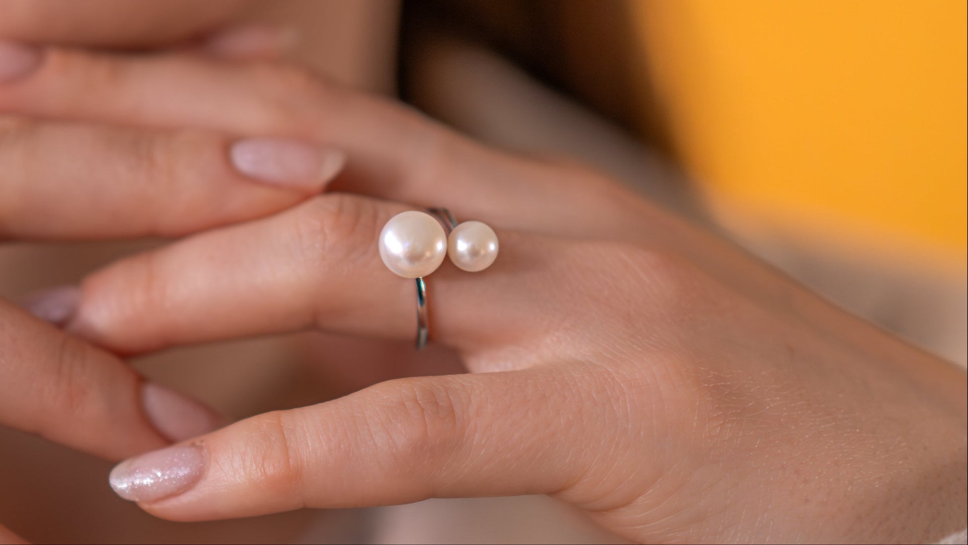 Close-up of hands wearing pearl rings with a blurred background