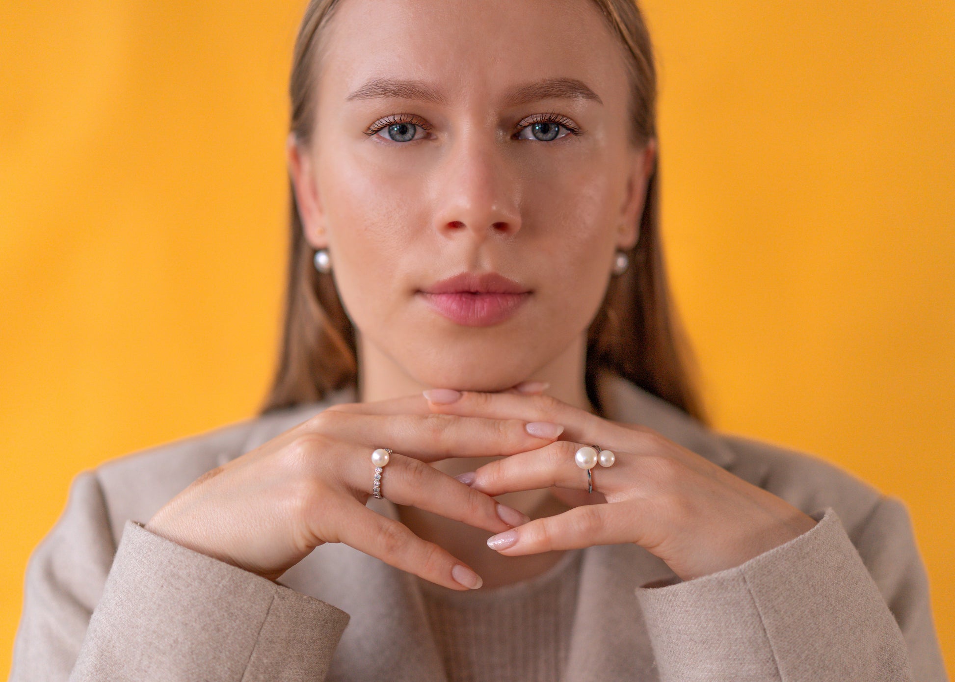 Woman wearing earrings and pearl rings against a yellow background
