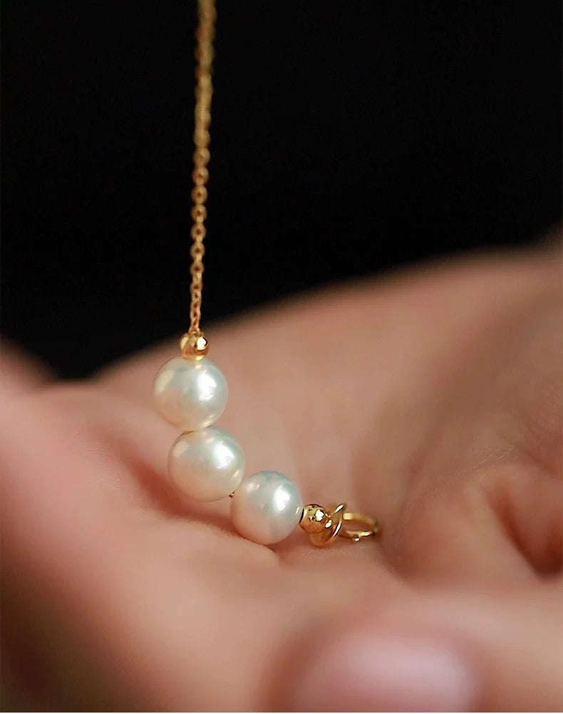 Pearl necklace with gold chain held in a hand against a dark background