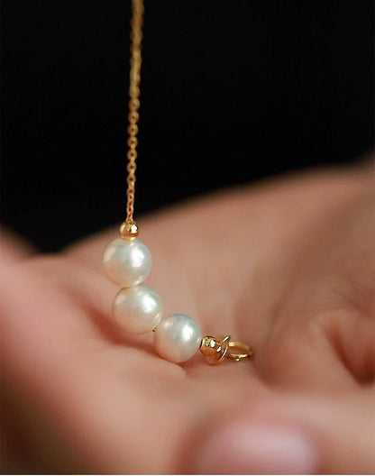 Pearl necklace with gold chain held in a hand against a dark background