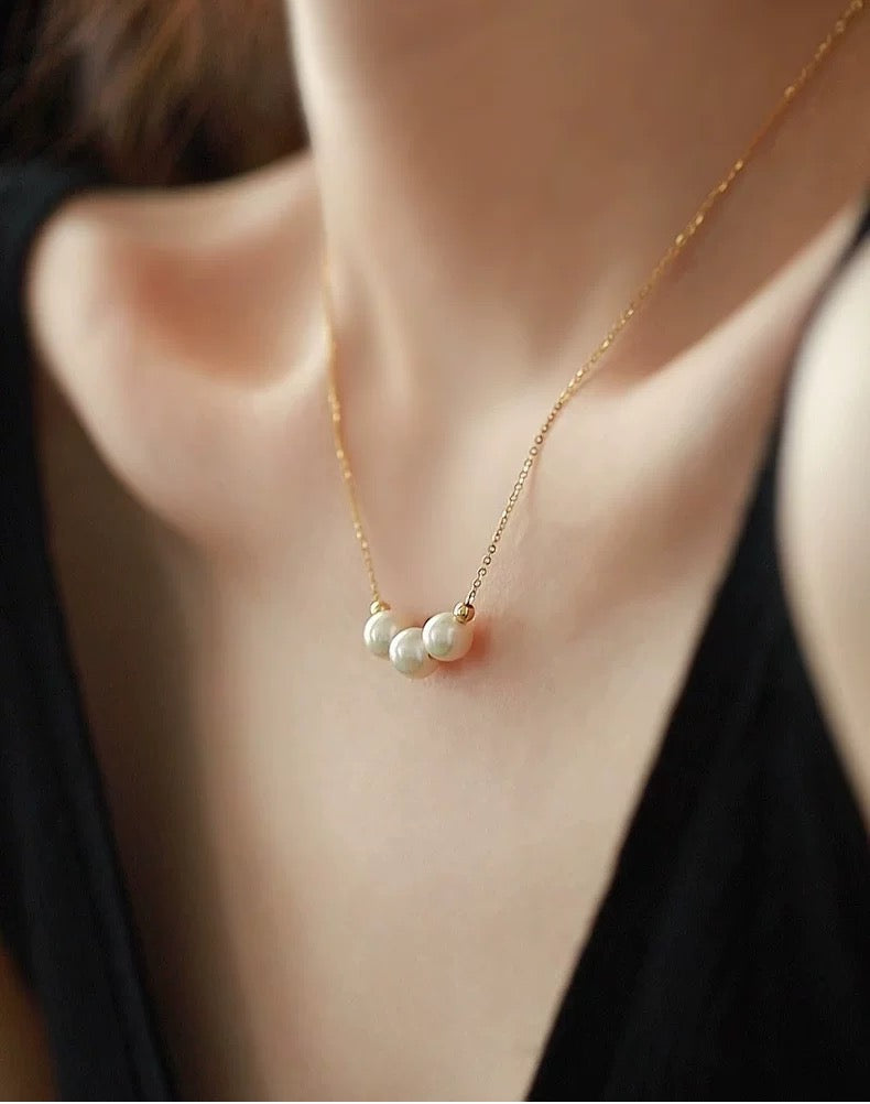 Gold necklace with three pearls worn by a person