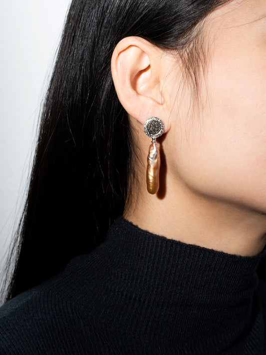 Close-up of a person wearing hoop pearl earrings with a black stone.