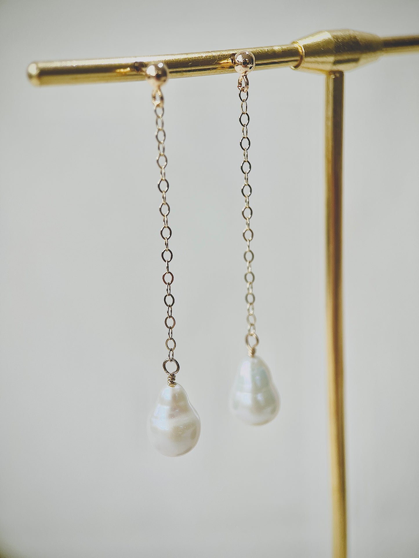 Pearl drop earrings hanging on a gold stand against a neutral background