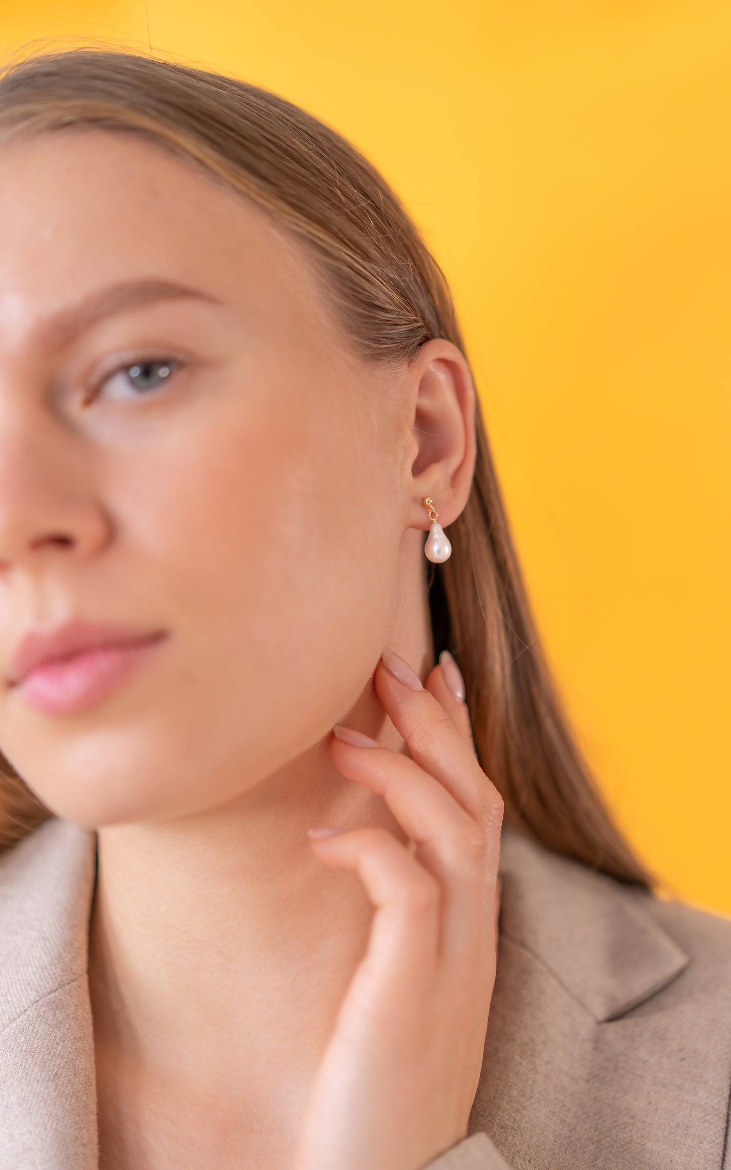 Woman wearing a gold pearl earring with a yellow background