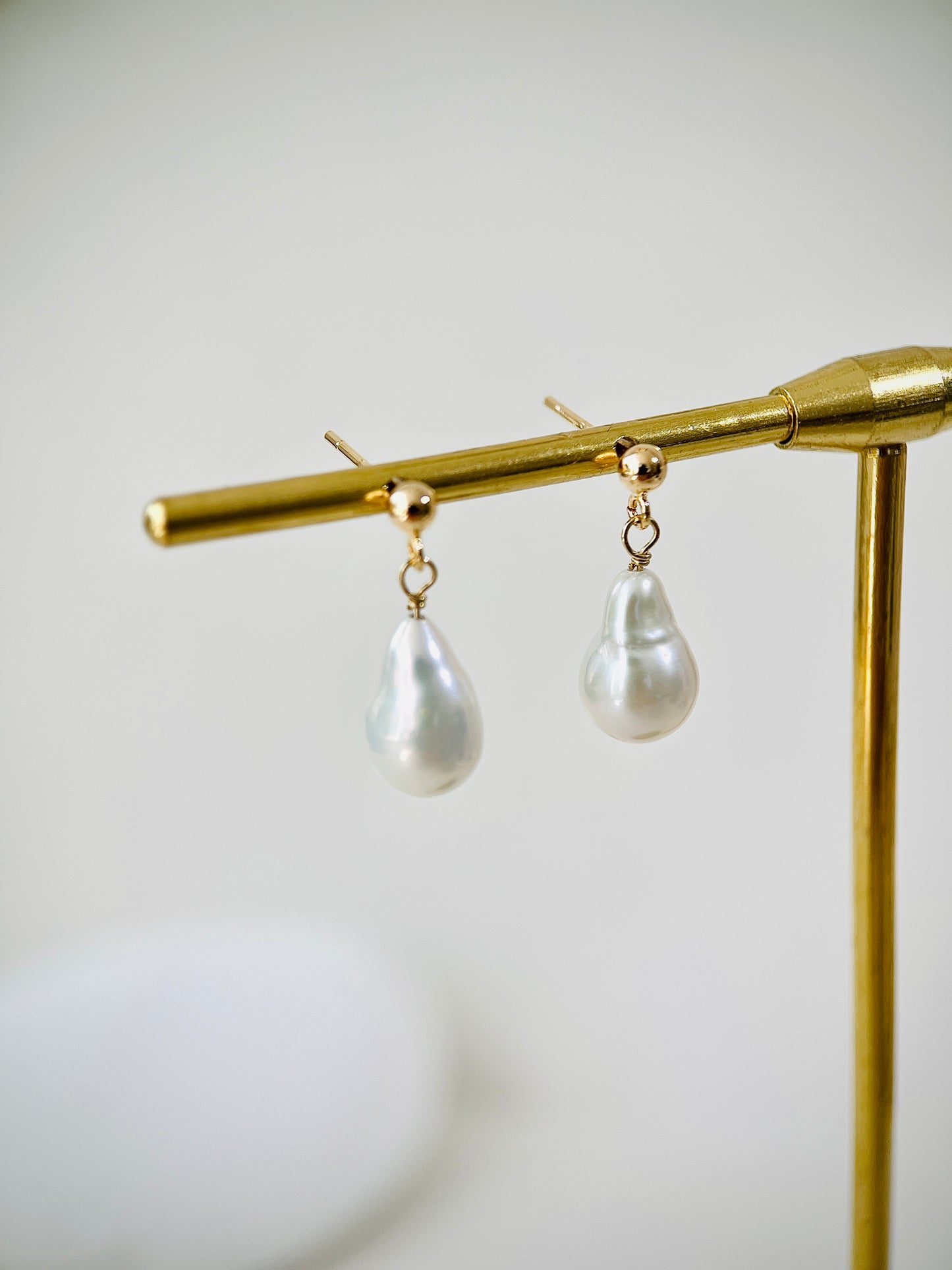 Pearl earrings hanging on a gold stand against a white background